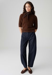 Maglione marrone peloso in maglia con maniche corte e dettaglio con fiocco, abbinato a jeans denim a gamba larga blu scuro e scarpe slip-on in camoscio marrone.