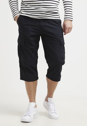 Granatowe cargo szorty z wieloma bocznymi kieszeniami, sięgające do kolan, o luźnym kroju, zestawione z białymi tenisówkami.