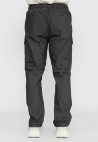 Pantaloni cargo grigio scuro con vita elastica, caratterizzati da tasche laterali e una vestibilità comoda. Indossati con scarpe da ginnastica chiare.