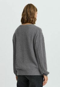 Grau gestrickter Pullover mit gerippten Akzenten, strukturiertem Stoff, lockerer Passform und überschnittenen Schultern. Verfügt über einen weitem Ausschnitt und ein Zopfmuster.