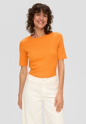 Haut orange à manches courtes en tissu côtelé, associé à un pantalon ample écru, présentant un col rond et une coupe ajustée.