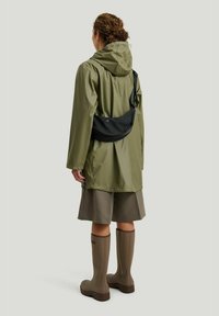 Olivengrøn vandtæt jakke med hætte, parret med en sort crossover taske, grå nederdel og beige knæhøje gummistøvler.
