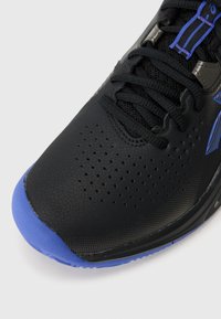 Baskets noires de sport avec une finition texturée, dotées d'un capuchon de protection en caoutchouc bleu et de détails perforés sur la tige pour une meilleure respiration.