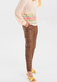 Bruna skinnbyxor matchade med en pastellfärgad tröja med flerfärgade horisontella randar och strukturerad stickad mönster. Klara gula sandaler.