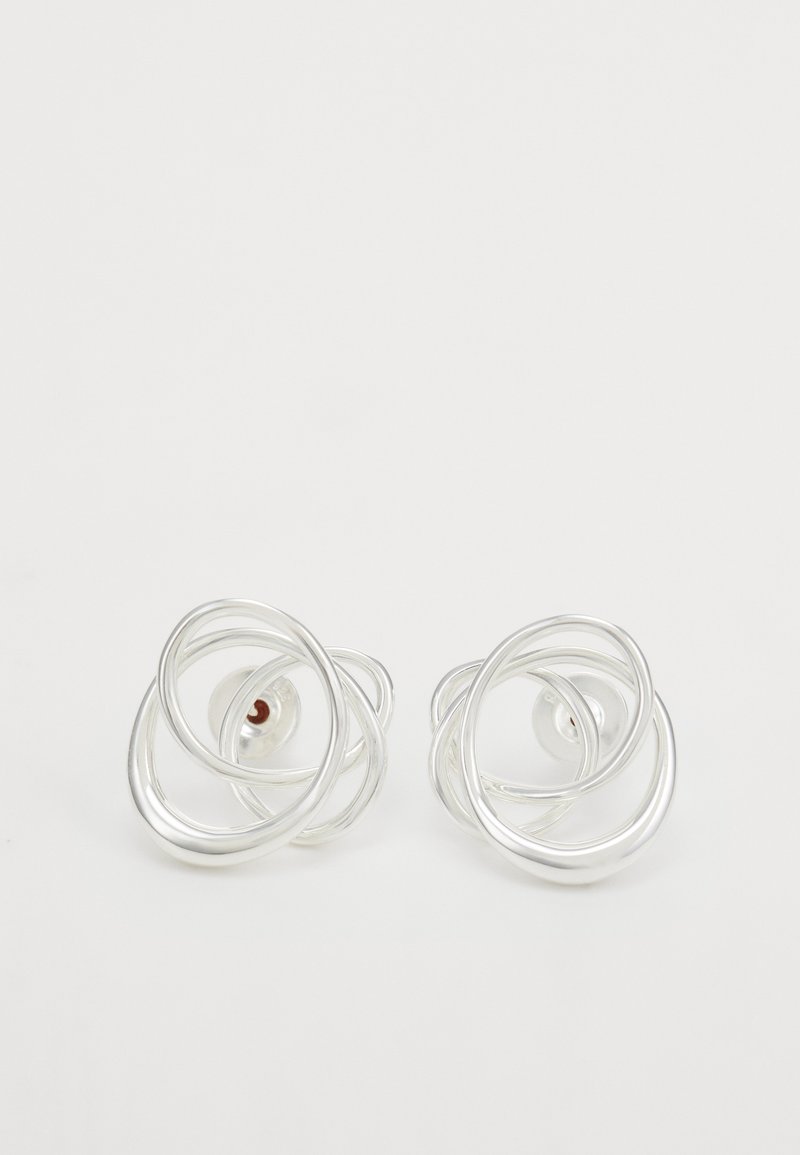 Srebrni kovinski uhani v obliki studov z abstraktno spiralo z več zankami in majhno rdečo podrobnostjo na hrbtni strani.