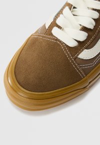 Hnědé semišové tenisky s krémovými tkaničkami, gumovou podrážkou, bílými pruhy a kontrastním šitím. Zaoblený tvar špičky.