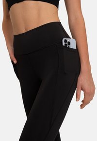 Zwarte sportleggings met een hoge tailleband, voorzien van een zijzak voor een smartphone. Glad textuur en platte stikdetails zichtbaar.