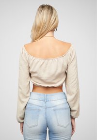 Top corto beige a spalle scoperte con maniche lunghe, caratterizzato da tessuto testurizzato e bordo elastico, abbinato a jeans a vita alta blu chiaro.