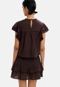 Brązowa, warstwowa sukienka z falbanowymi rękawami i dołem. Posiada dekolt w kształcie łezki z tyłu oraz dekoracyjną lamówkę. Wykonana z lekkiego materiału.