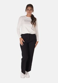 Camicia bianca a maniche lunghe con la scritta "YES" stampata in argento, abbinata a pantaloni neri a gamba dritta e sneakers bianche. Outfit semplice e casual.