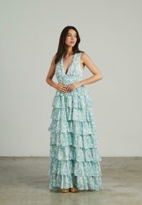 Vestido maxi con estampado floral, escote en V profundo, diseño sin mangas y volantes en capas en tonos de verde claro y azul, de tela texturizada.