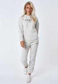 Lichtgrijze hoodie en bijpassende joggers van een zachte katoenmix, met een frontzak, logo prints en geribde manchetten; gecombineerd met witte sneakers.