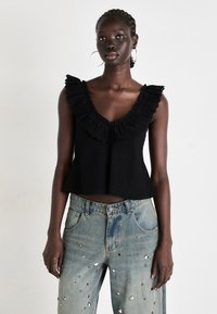 Black sleeveless top with a ruffled neckline; paired with distressed light blue jeans featuring metallic embellishments and a relaxed fit.