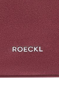 Nahaufnahme einer strukturierten, kastanienbraunen Oberfläche mit weißen Großbuchstaben "ROECKL", die nahe am unteren Rand zentriert sind.