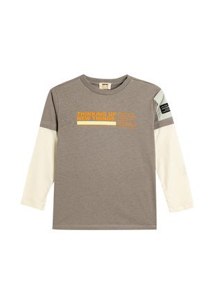 T-shirt gris à manches longues avec des manches blanches, arborant un texte orange "THINKING UP NEW THINGS" et une étiquette noire sur l'épaule. Matière en coton doux.
