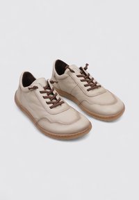 Beige leather sneakers with brown laces, rounded toe, and textured surface. Rubber sole with a subtle tread design. Modern, casual style.