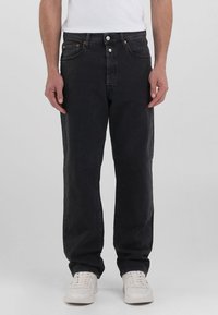 Schwarze Denim-Jeans mit geradem Schnitt, ausgestattet mit fünf Taschen, einem Knopfverschluss und dezenten orangen Nähakzenten. Getragen mit weißen Sneakers.