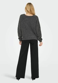 Pilkas, pūkuotas megztinis su laisvu siluetu ir per didelėmis rankovėmis, derinamas su juodomis plačiomis kelnėmis su aukštu liemeniu ir bateliais ant storos pakulnės.