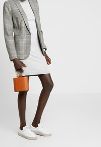Blazer a quadri grigio e nero con accenti gialli; vestito maglione grigio chiaro; borsa arancione con texture coccodrillo; sneaker bianche.