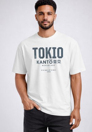 Man with beard wearing white T-shirt that reads "TOKIO KANTO" with Japanese characters, coordinates, and "NEVERLESS" text, posing against plain background.