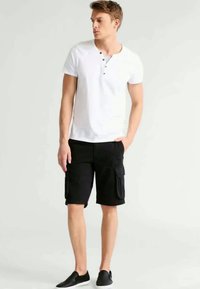 White short-sleeve henley shirt with a buttoned neckline, paired with black cargo shorts featuring side pockets and flat black slip-on shoes.