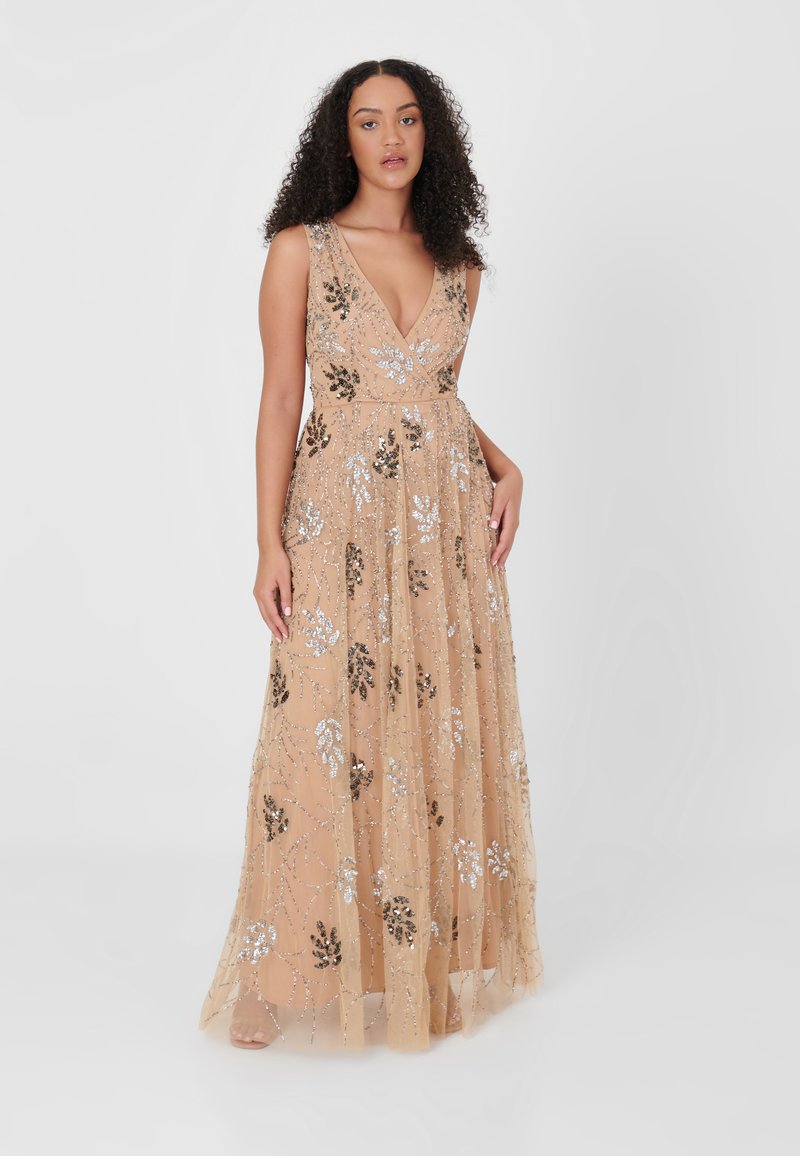 Vestido largo, beige, con un escote en V profundo, adornado con patrones florales en plata y negro y lentejuelas. Tela transparente y fluida que cae hasta el suelo.