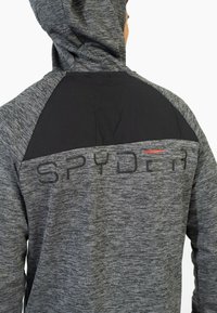 Giacca grigia con cappuccio e finitura testurizzata, dotata di un pannello superiore nero solido e della parola "SPYDER" in lettere nere sulla schiena.