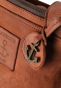 Braune Lederhandtasche mit strukturiertem Oberflächenmaterial, versehen mit einem Metall-Anker-Anhänger und gestickten Designelementen. Reißverschlussverschluss an der Oberseite.