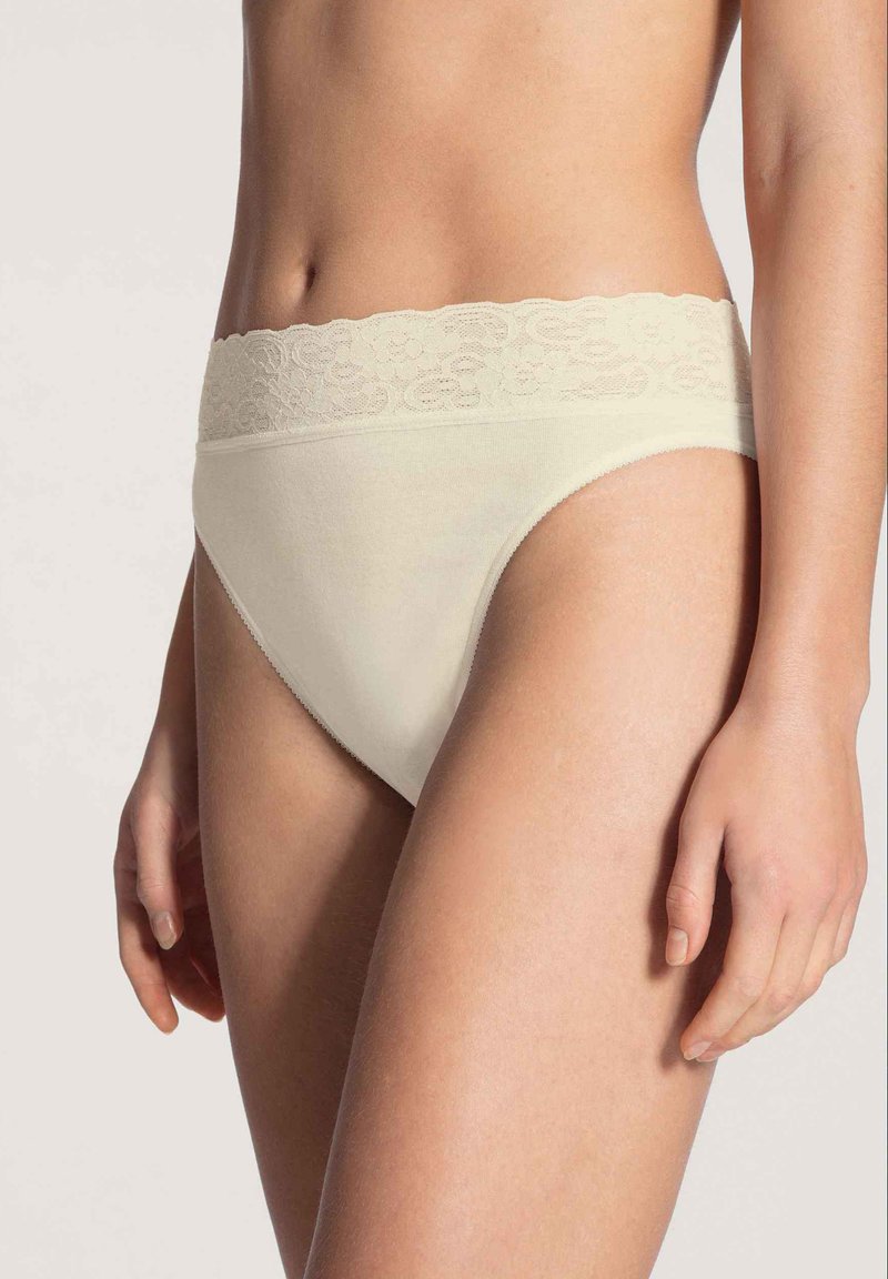 Beige Baumwollunterwäsche mit einem Spitzenbund, ausgestattet mit einem hohen Beinausschnitt und glatter Textur, ideal für Komfort und den alltäglichen Gebrauch.