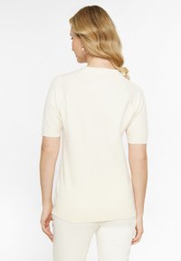 Lyse beige kortærmet top i et blødt, tekstureret strik. Har en rund halsudskæring og en lidt længere bagkant, parret med matchende lyse bukser.