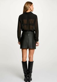 Camicia nera trasparente a maniche lunghe con un delicato motivo a righe, abbinata a una mini gonna in pelle nera e stivali neri con tacco al ginocchio.