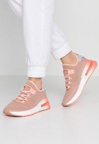 Ljusrosa träningsskor med en ventilerande meshövre, kontrasterande grå detaljer och en synlig vadderad sula, designad för komfort.