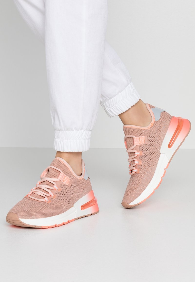 Ljusrosa träningsskor med en ventilerande meshövre, kontrasterande grå detaljer och en synlig vadderad sula, designad för komfort.