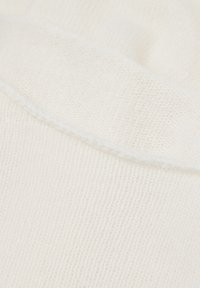 Primo piano di un tessuto lavorato a maglia morbido e bianco con cuciture visibili lungo il bordo piegato, che mette in risalto la texture e il dettaglio della trama.