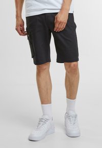 Pantaloni cargo neri con tasche laterali, realizzati in tessuto morbido, caratterizzati da una vestibilità rilassata e dettagli di cucitura discreti, abbinati a sneakers bianche.