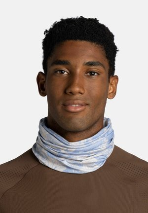 Young man with short curly hair wearing a brown top and a light blue patterned neck gaiter against a plain white background.