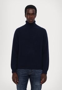 Marineblauer Rollkragenpullover aus weichem Strickstoff, mit langen Ärmeln, gerippten Bündchen und einem lässigen Schnitt, kombiniert mit blauen Jeans.
