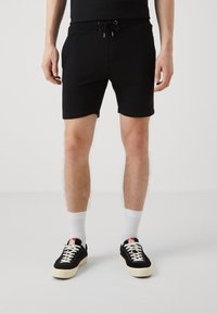 Sorte shorts i bomuldsblanding med elastisk talje og snor. Har en tætsiddende pasform og syet kant. Bæres med sorte sneakers og hvide sokker.