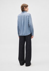 Světlomodrá košile s dlouhými rukávy, límečkem a záhybem na zadní straně, doplněná o široké tmavomodré džínové kalhoty.