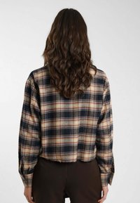 Camicia a quadri cropped in nero, marrone e beige. Caratterizzata da maniche lunghe, vestibilità ampia e una texture del tessuto con una finitura morbida.