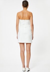 Vestido blanco sin mangas con un cuerpo ajustado, borde de encaje en el escote y dobladillo recto. Textura suave y detalle de cremallera en la parte posterior.
