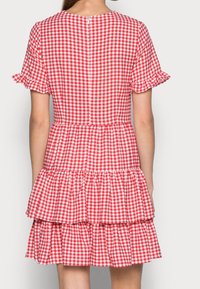 Robe vichy rouge et blanche avec de courtes manches à volants, jupe à étages et fermeture à boutons dans le dos. Tissu en coton, design décontracté.