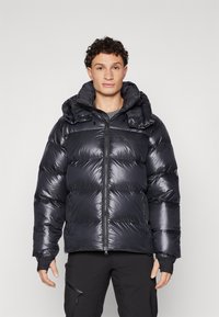Must have puffer-jakk musta läikiva materjaliga, tikitud disain ja suur kapuuts. Omab eesmine tõmblukk ja elastsed mansetid soojuse tagamiseks.