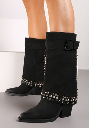 Des bottines noires en daim avec un large revers, une boucle décorative et une rangée de clous le long du bord inférieur. Bout pointu et talon carré.
