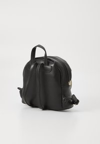 Le sac à dos en simili cuir noir présente une forme arrondie, deux poignées supérieures, des bretelles réglables et une fermeture éclair avec quincaillerie dorée.