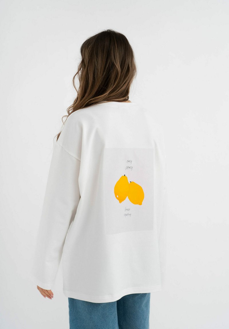 Witte sweatshirt met lange mouwen, voorzien van een gele citroenafbeelding op de achterkant. Zacht materiaal en een relaxte pasvorm, eenvoudige voorkant.