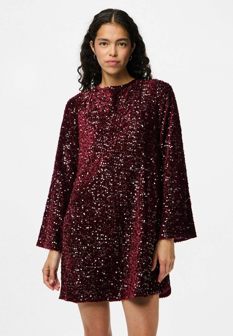 Bordo haljina sa sequinskim detaljima, dugim rukavima, okruglim izrezom i slobodnim fitom. Tkanina ima sjajnu, teksturiranu površinu zbog preklapanja sequina.