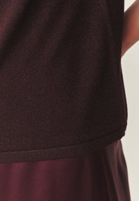 Pull bordeaux avec une finition en maille texturée, présentant un ourlet côtelé et des manches courtes, associé à une jupe bordeaux lisse.