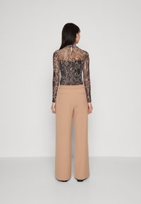 Svart og beige bodysuit med slangeskinnmønster, lange ermer og høy hals, kombinert med brede beige bukser.