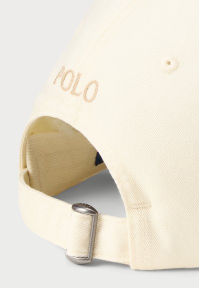 Krēms krāsas beisbola cepure ar izšūtu "POLO" bēšā krāsā. Izgatavota no teksturētas kokvilnas materiāla un aprīkota ar regulējamu metāla siksniņu aizmugurē.